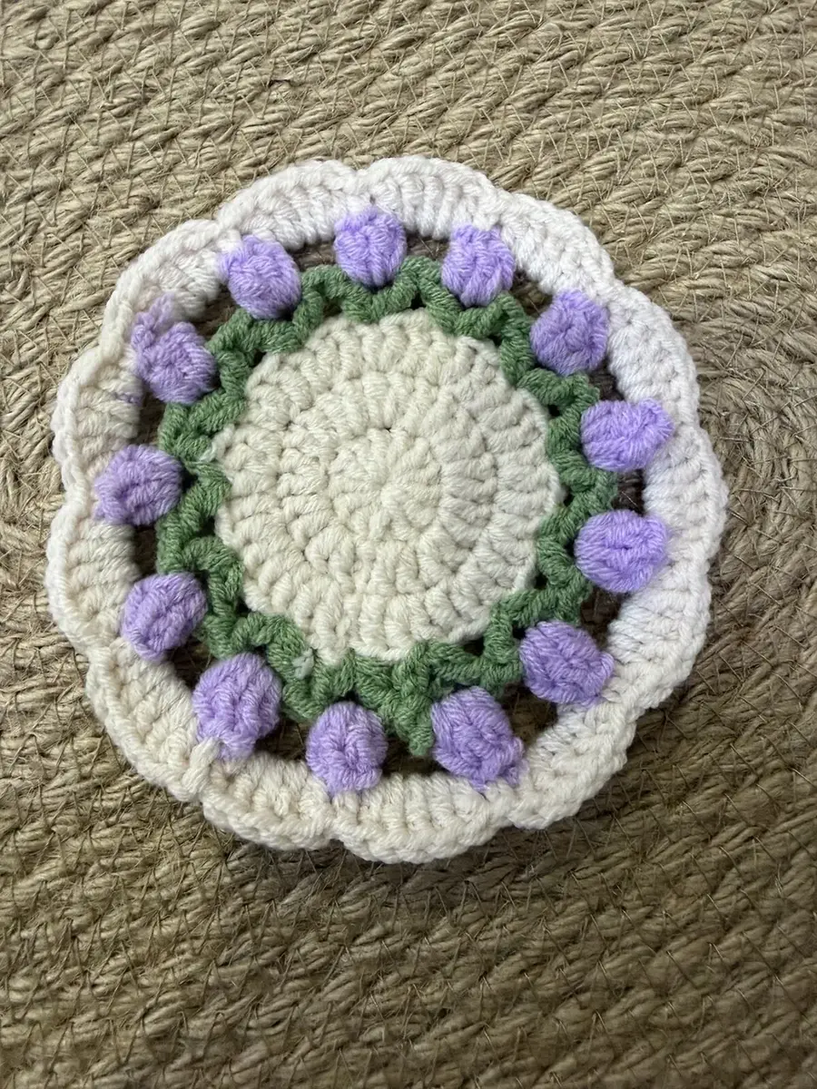 A flower coaster with purple puffs.
