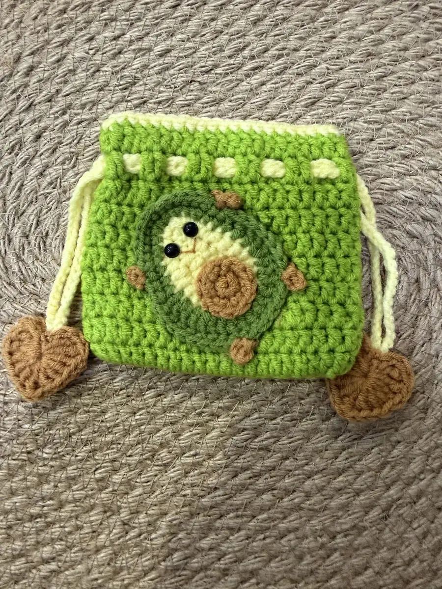 A green crochet avocado drawstring pouch with a brown pit and a smile.
