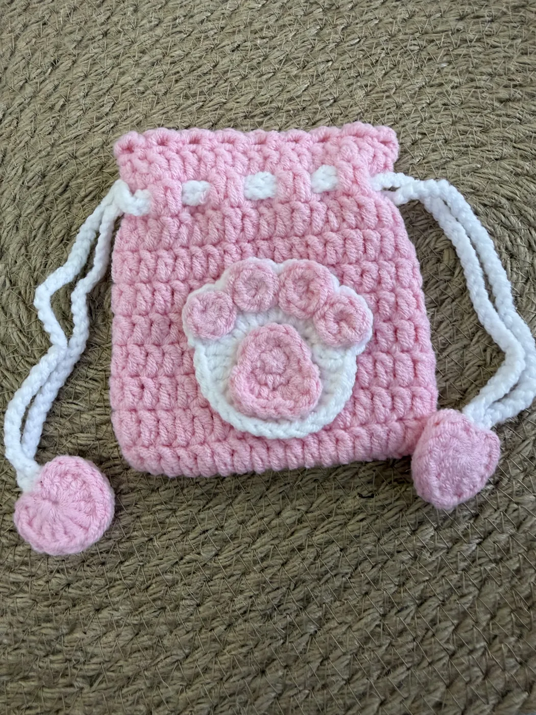 A pink crochet drawstring pouch with a paw face.