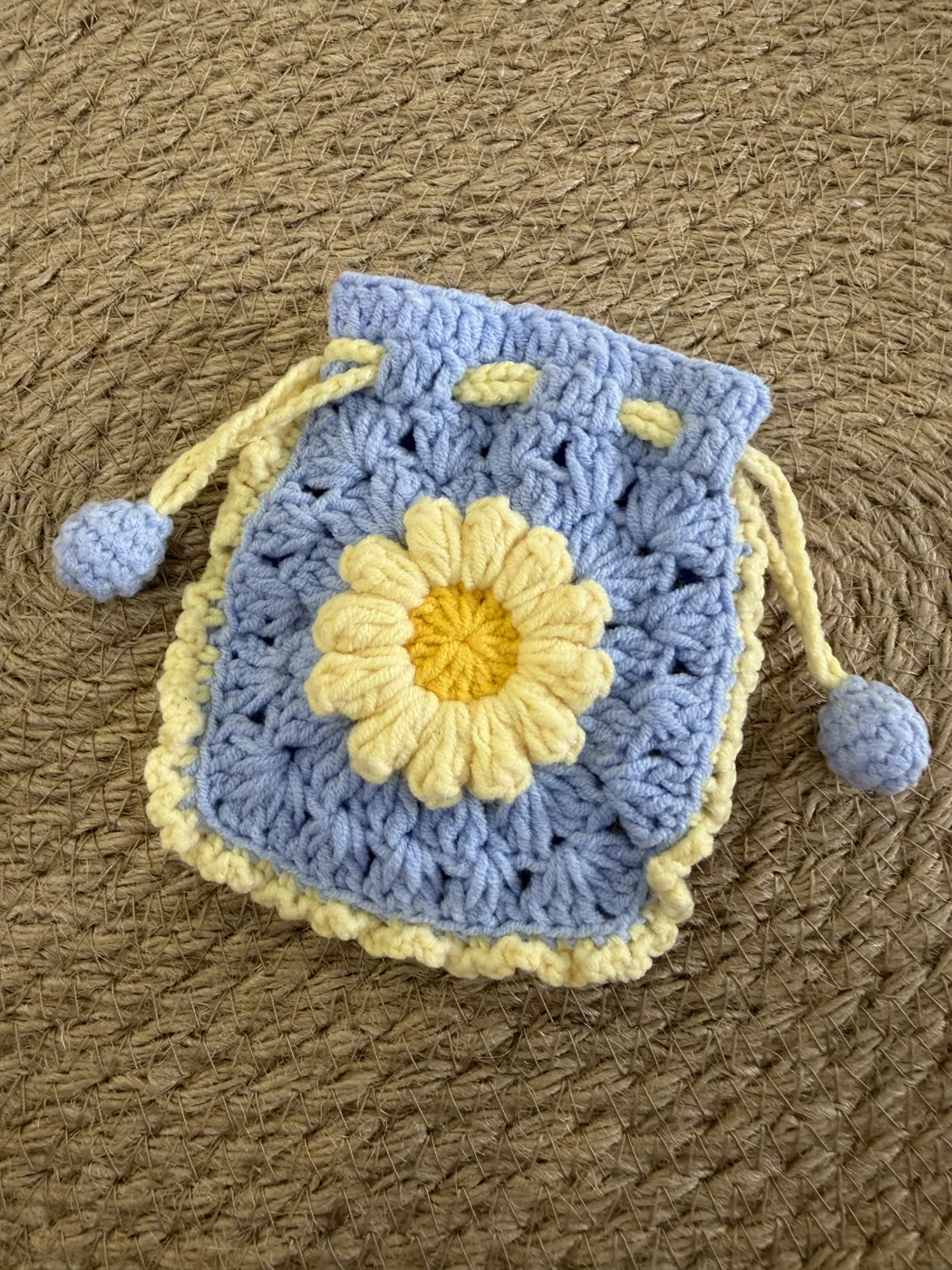 A blue crochet drawstring pouch with a yellow daisy.