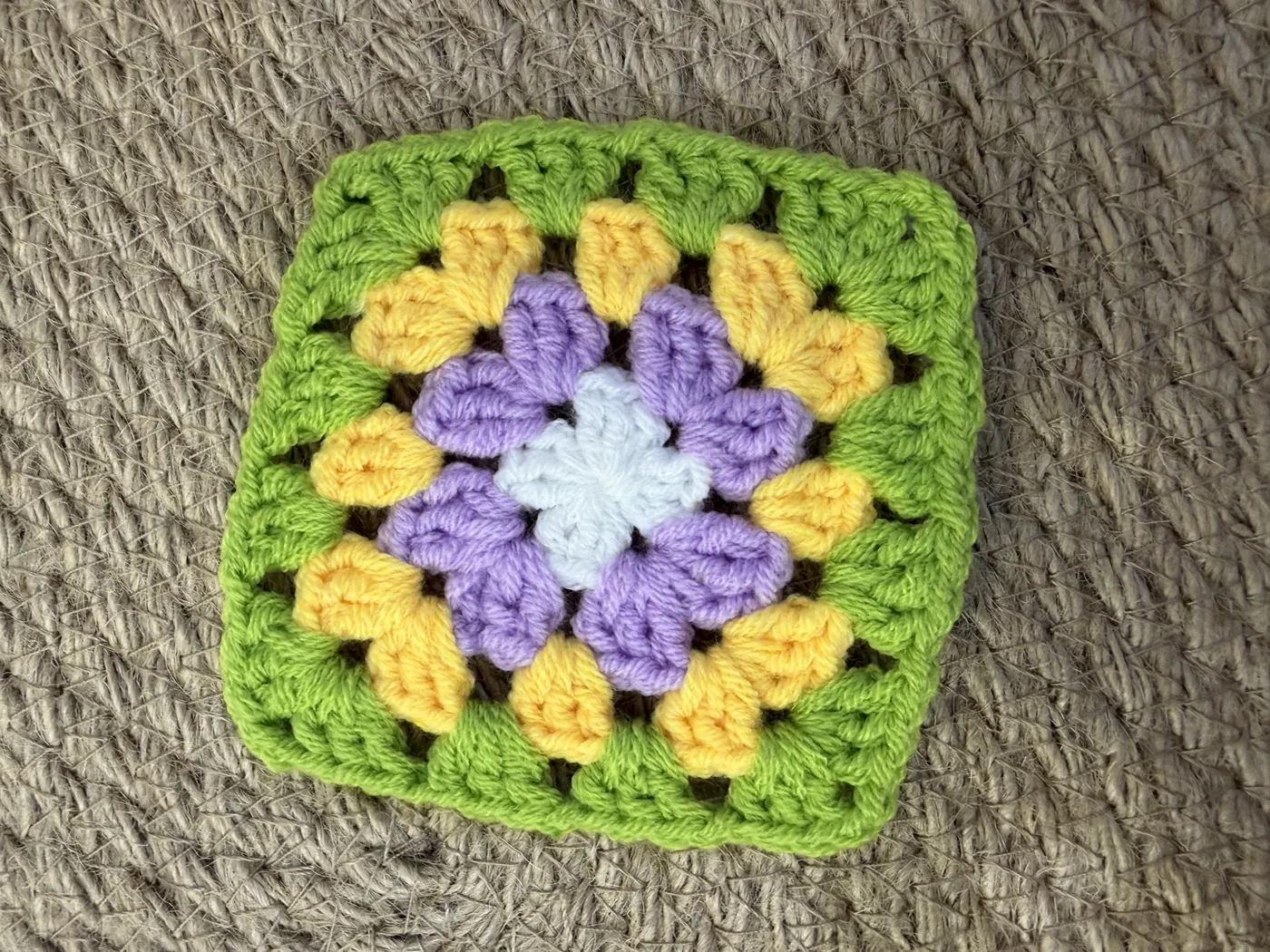 A crochet granny square in yellow, pink, blue and green.