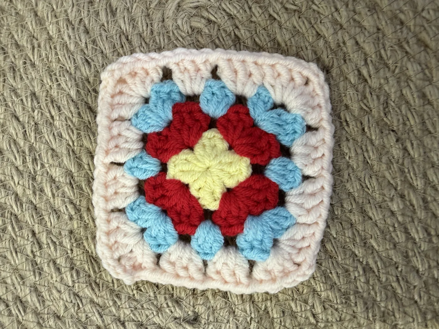 A crochet granny square in red, blue, pink and white.