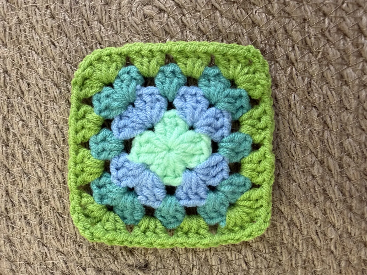 A crochet granny square in green, yellow and blue.